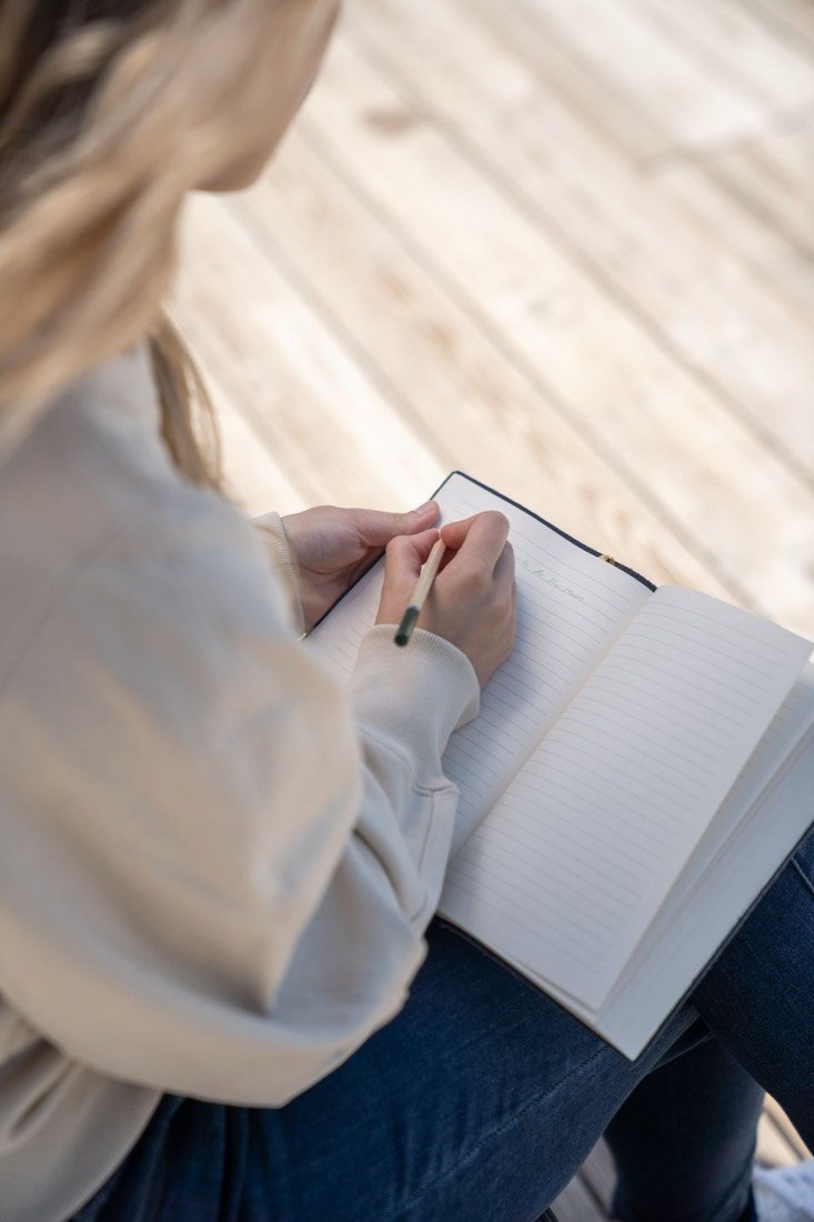 Una mujer joven escribe a mano en un cuaderno abierto sobre sus rodillas